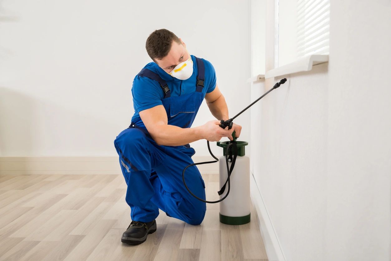 A man in blue overalls spraying water on the wall.